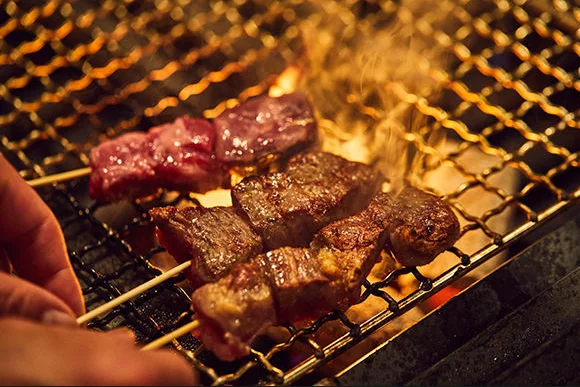 炭火の前で鶏肉の串を焼く調理スタッフの手元